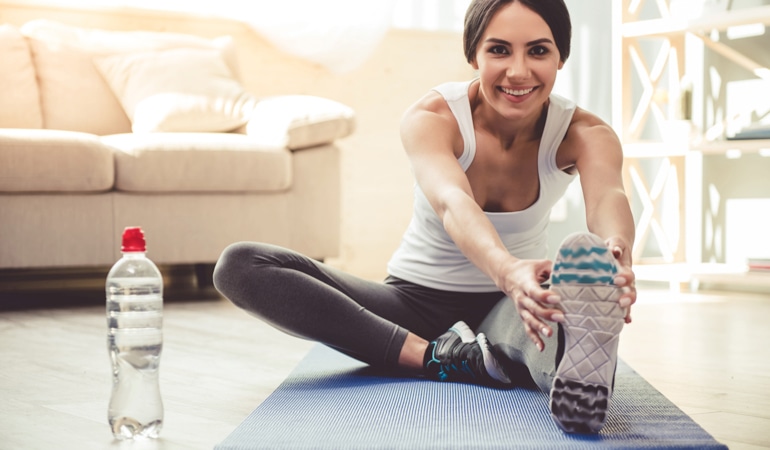 Женщина на коврике для йоги наклоняется вперед, выполняя растяжку мышц ног для профилактики венозной недостаточности.